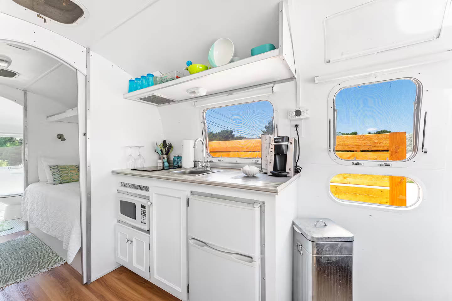 Interior kitchenette and sleeping space inside The Ellington Airstream at Glamp Newport Bright white kitchenette and sleeping area inside The Ellington vintage Airstream rental at Glamp Newport in Portsmouth Rhode Island